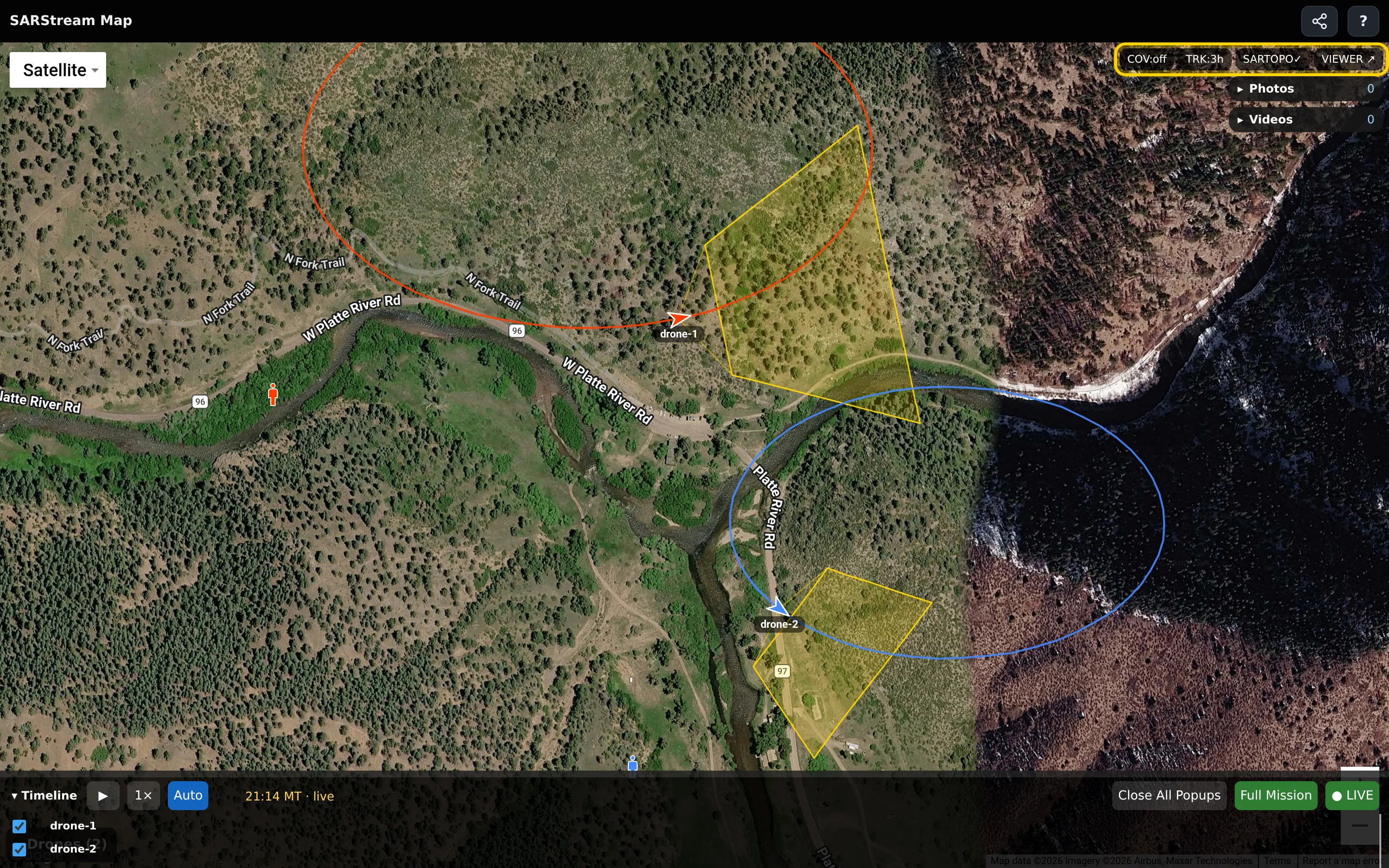 The full map page: two drones with their names, yellow camera boxes and trail lines on satellite imagery, the pilot marker, the timeline along the bottom, and the COV, TRK, SARTOPO and VIEWER buttons outlined at the top right